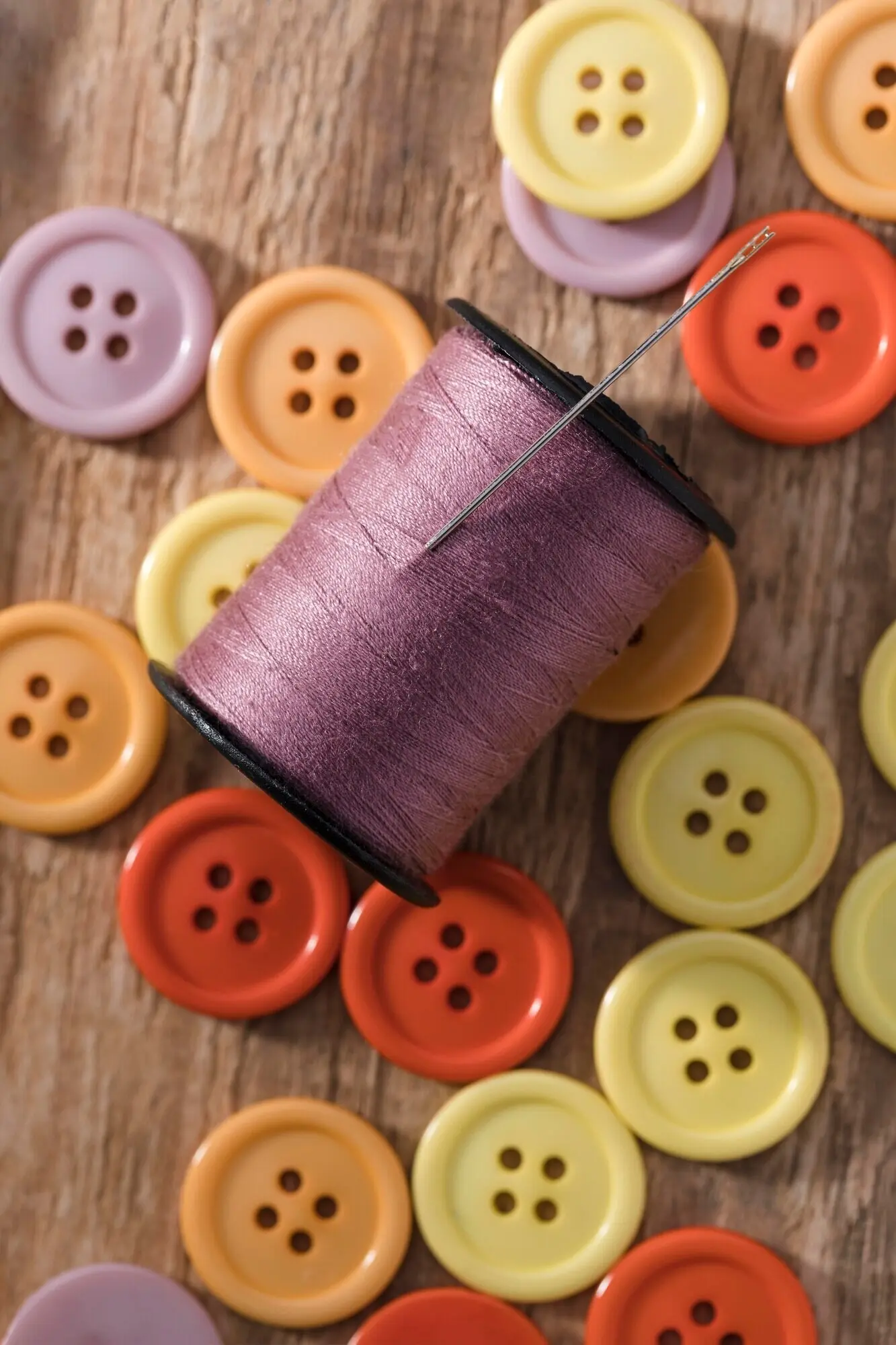 Draufsicht auf eine Garnrolle mit Knöpfen und einer Nähnadel